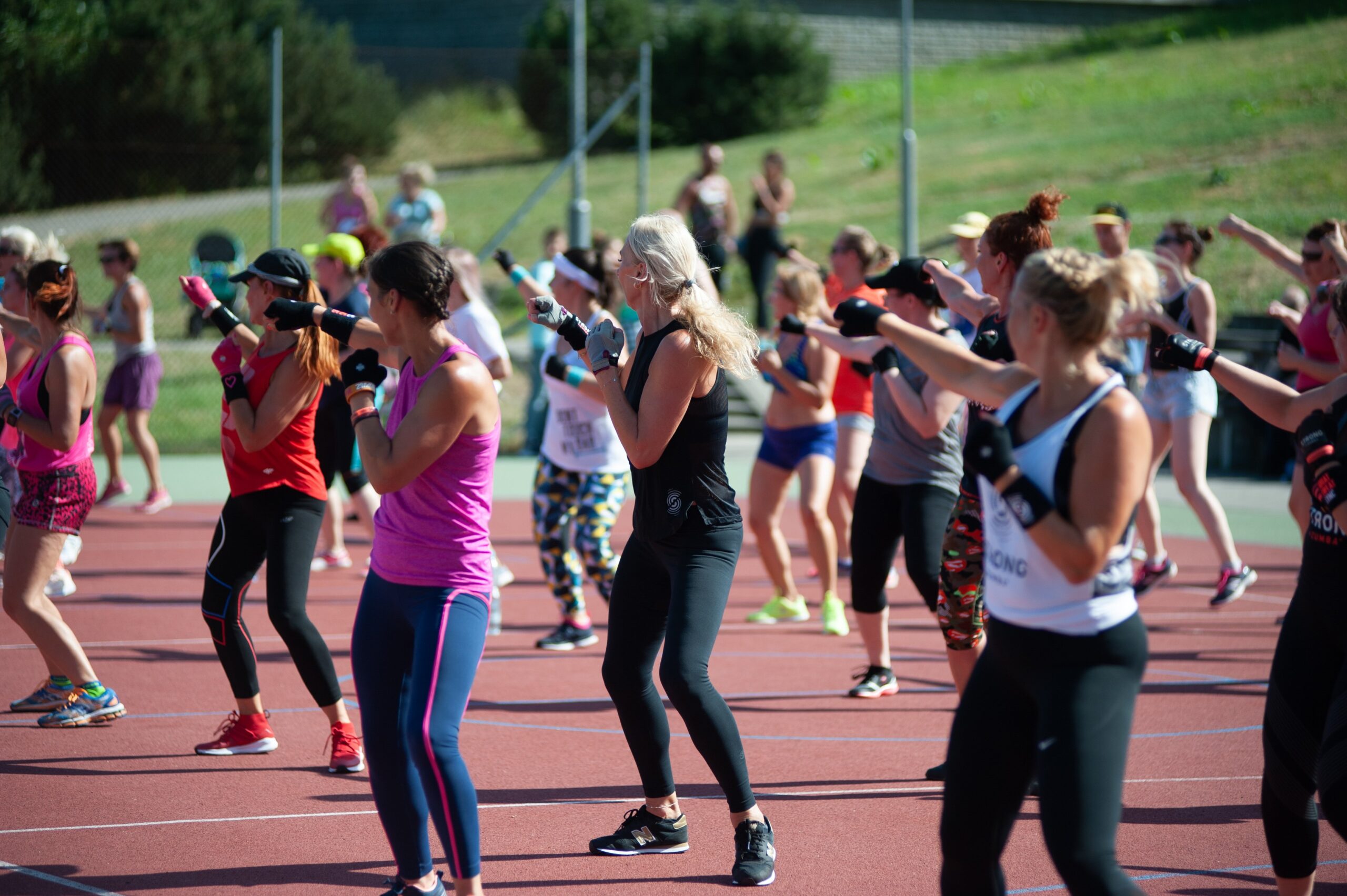 Large group of women doing outdoor aerobics and cardio kickboxing class together on a track — group fitness classes burn up to 680 calories per hour and boost motivation through community and shared energy